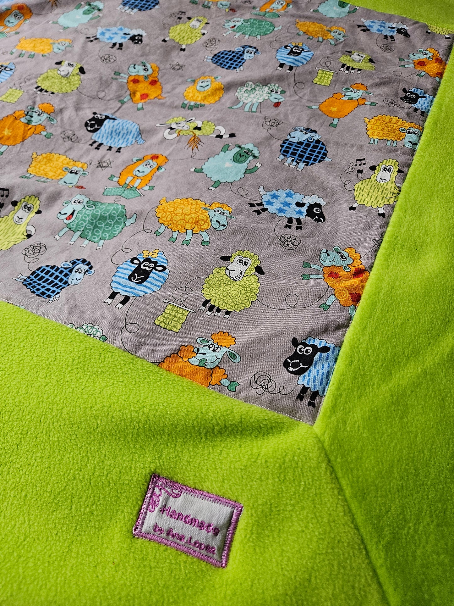 Fun Colourful Sheep's Handmade Blanket on Grey background. Double sided, cotton fabric in one side, and bright fluorescent green fleece at the back.