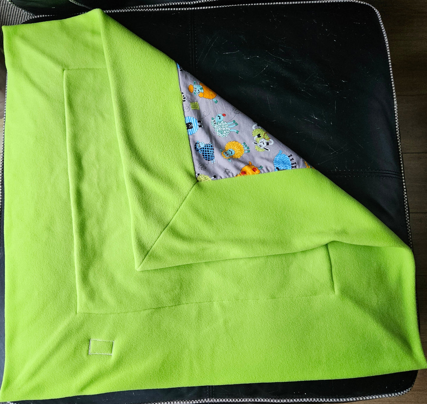 Fun Colourful Sheep's Handmade Blanket on Grey background. Double sided, cotton fabric in one side, and bright fluorescent green fleece at the back.