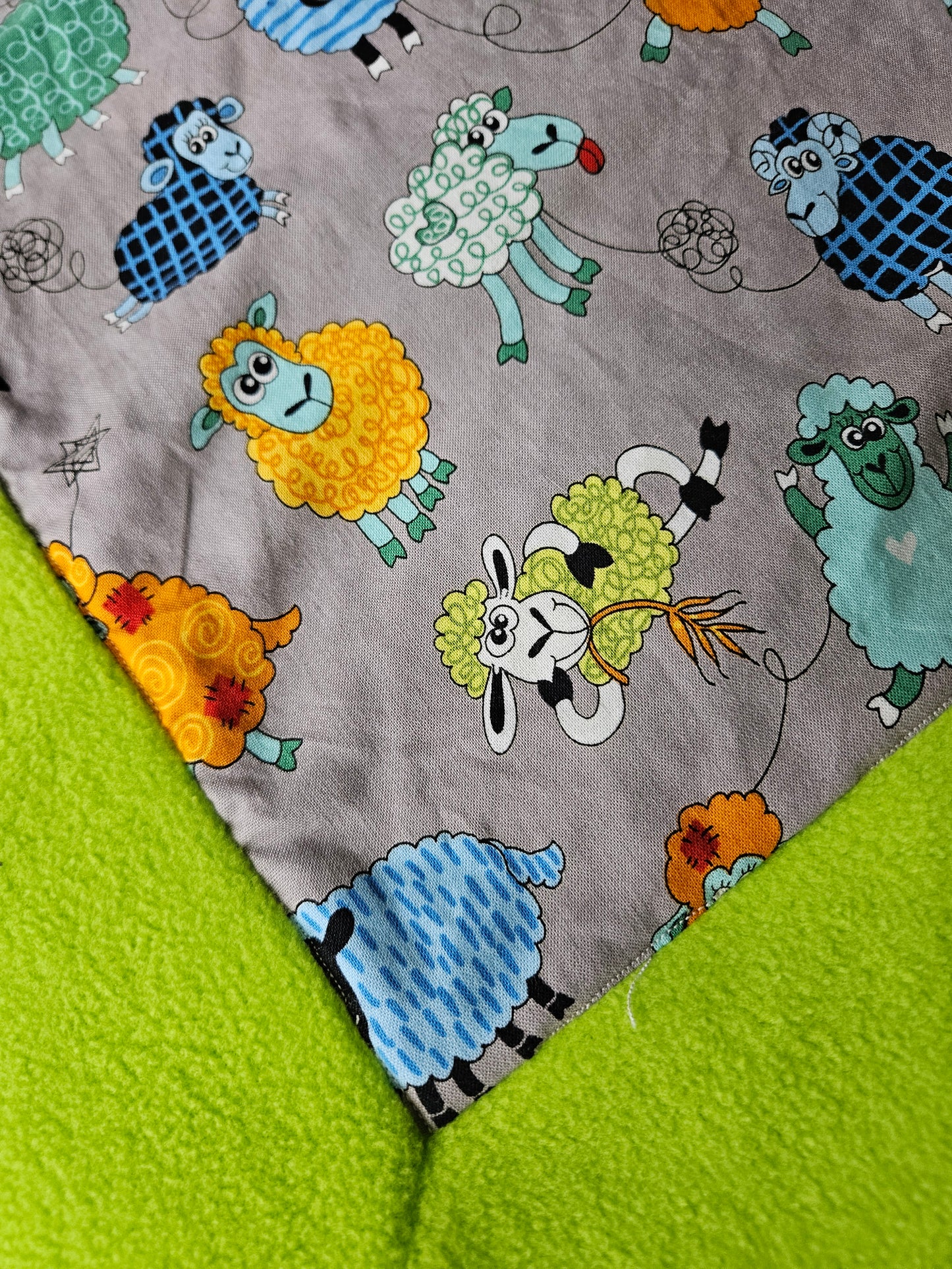 Fun Colourful Sheep's Handmade Blanket on Grey background. Double sided, cotton fabric in one side, and bright fluorescent green fleece at the back.