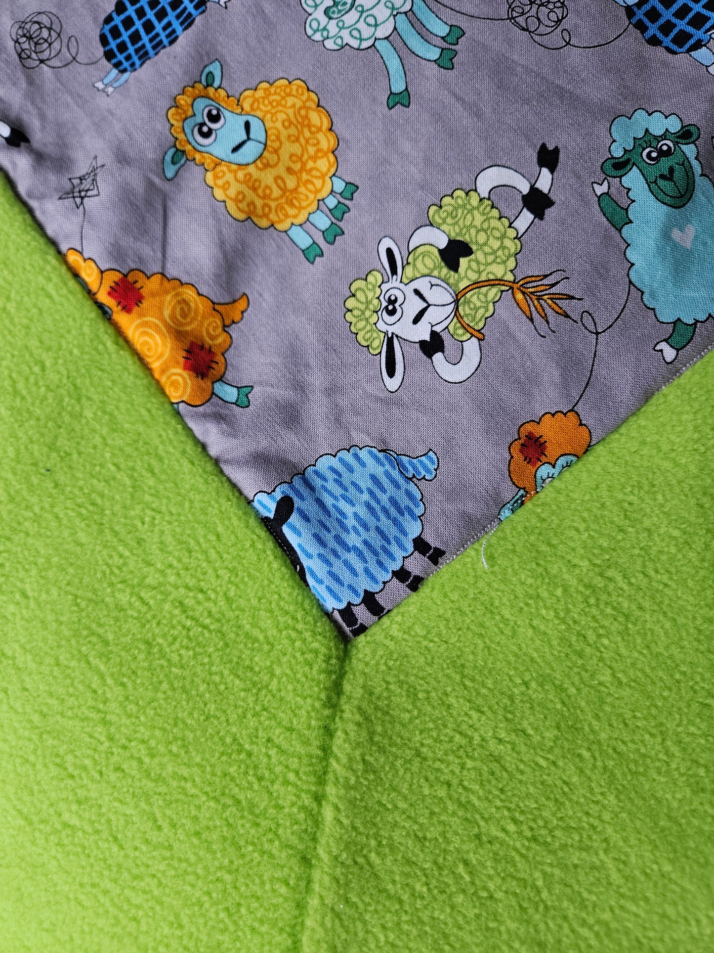 Fun Colourful Sheep's Handmade Blanket on Grey background. Double sided, cotton fabric in one side, and bright fluorescent green fleece at the back.