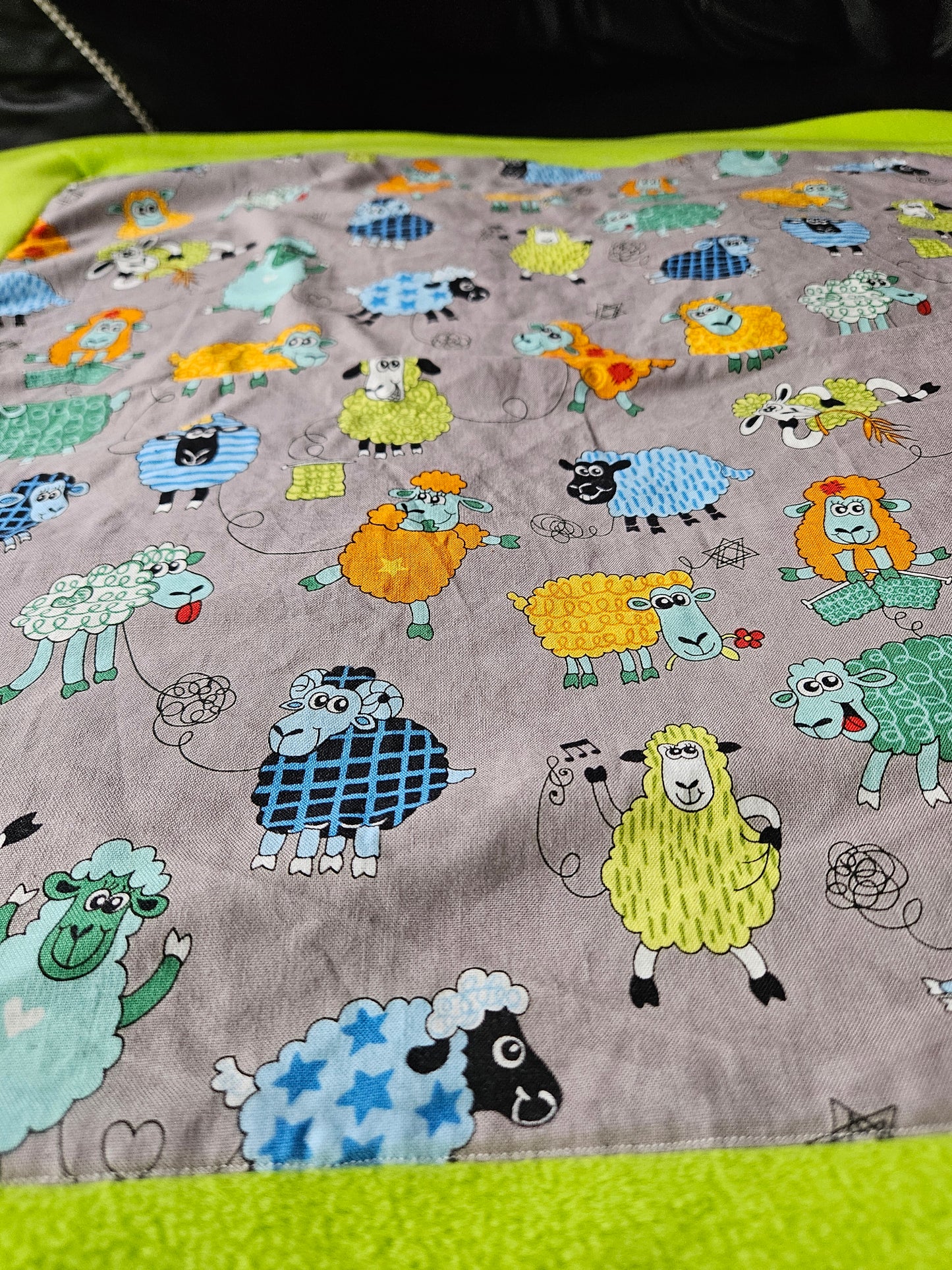 Fun Colourful Sheep's Handmade Blanket on Grey background. Double sided, cotton fabric in one side, and bright fluorescent green fleece at the back.