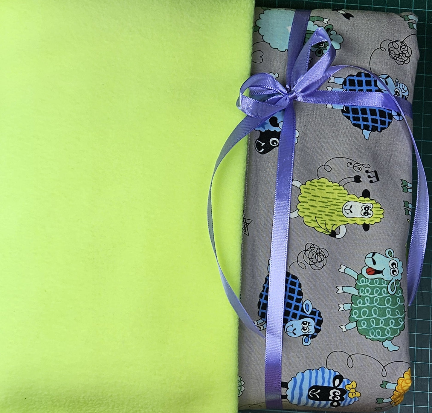 Fun Colourful Sheep's Handmade Blanket on Grey background. Double sided, cotton fabric in one side, and bright fluorescent green fleece at the back.